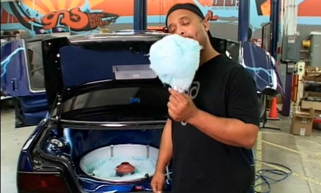 A guy eating cotton candy from a cotton candy machine located in the front hood of the car