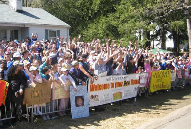 A croud of people with raised hands holding banners up that containe messages welcoming someone to their new home.