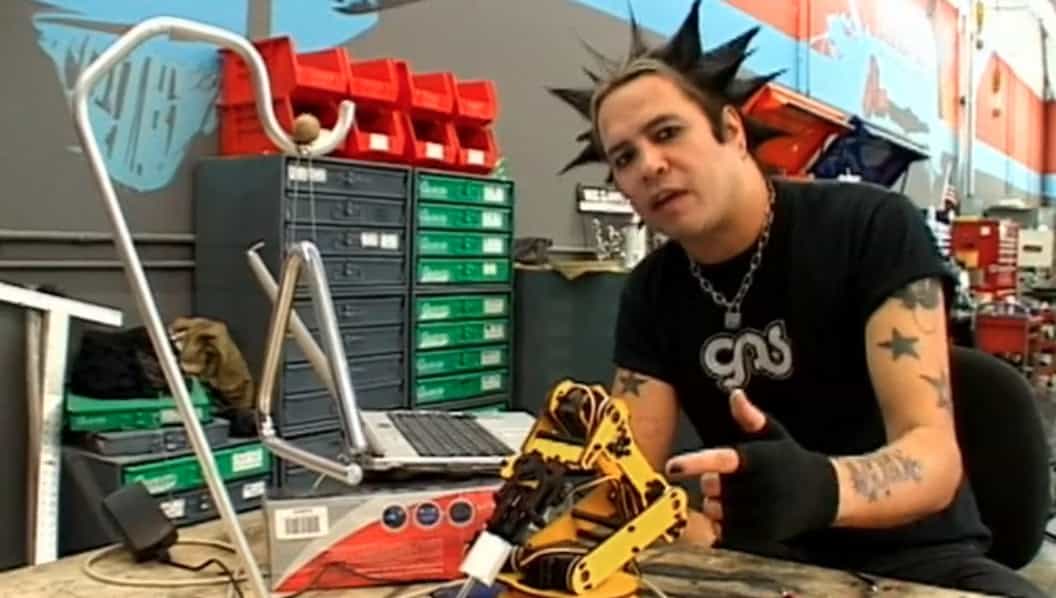 A guy with a mohawk and tatoos sitting by a desk